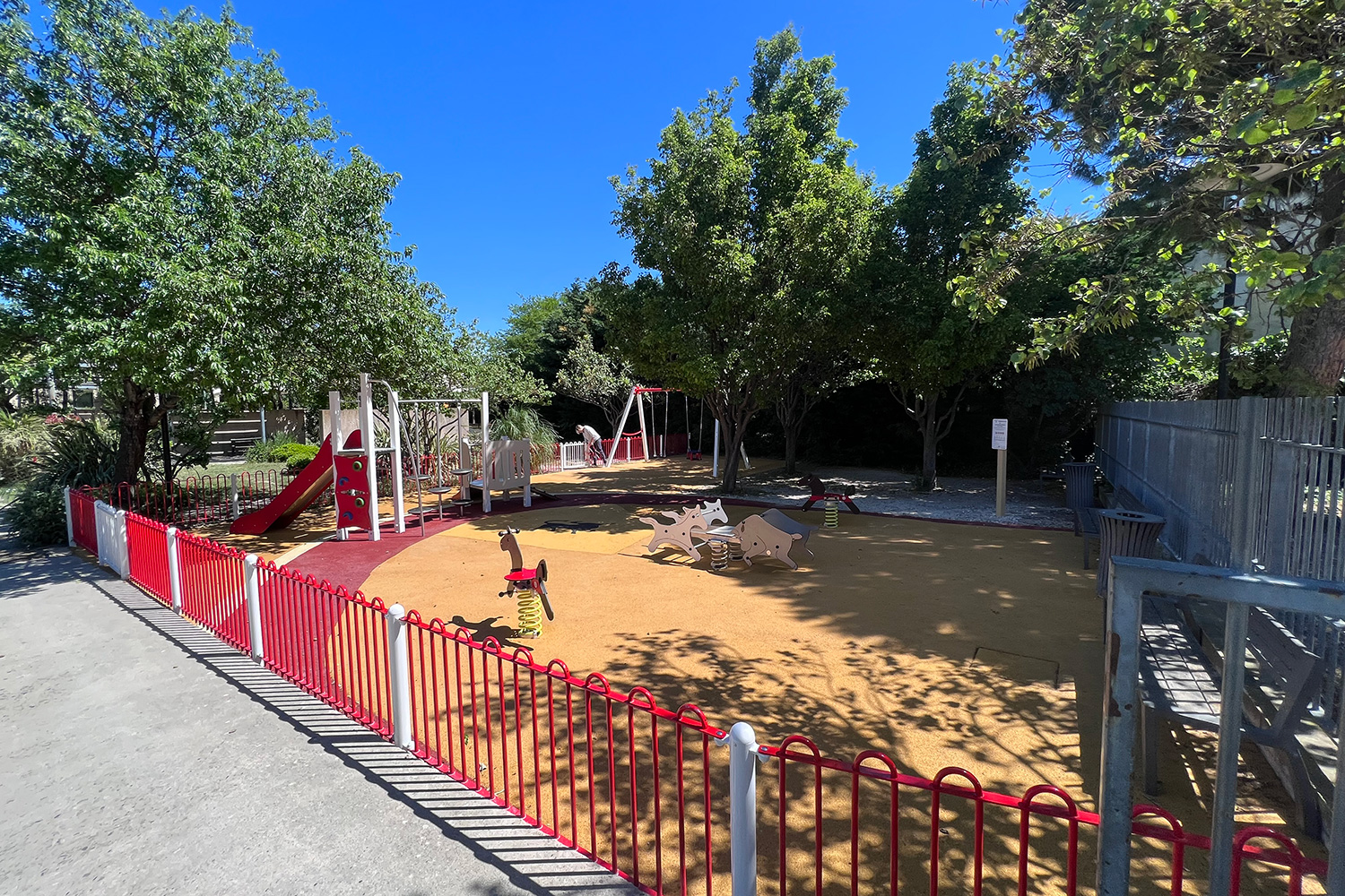 Aire de jeux avec revêtement de sol amortissant orange et clôture de sécurité rouge